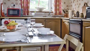 A kitchen with a dining table set, a microwave, a sink, and a window with curtains.