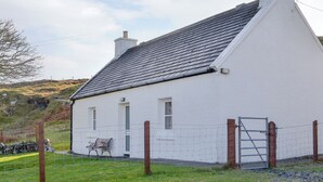 A white house with a grey roof, a chimney, and a small porch with a bench.