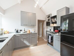 A modern kitchen with grey cabinets, a black refrigerator, and a wooden floor.