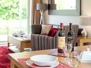 A dining table with two wine bottles, a glass, and a white bowl set on a red placemat.