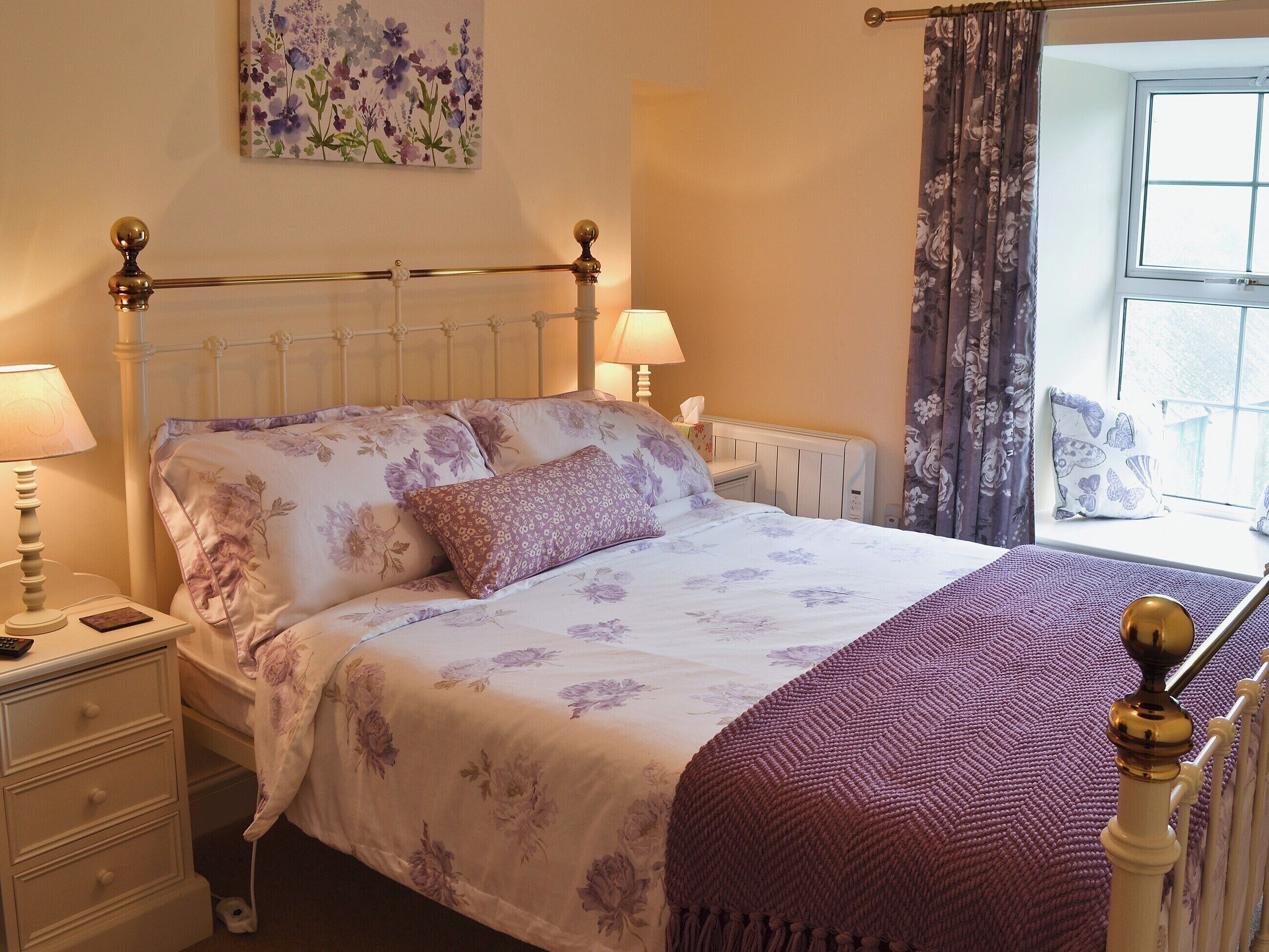 A neatly made bed with floral bedding, a bedside lamp, and a window with curtains.