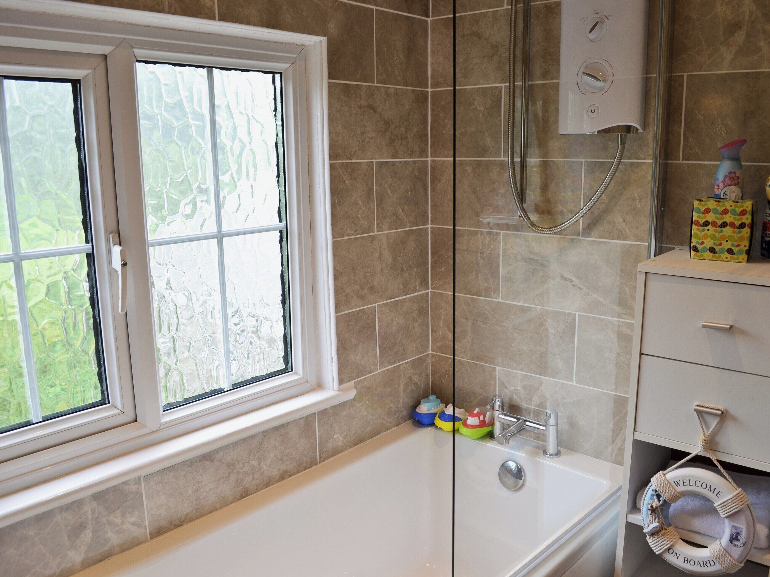 A bathroom with a bathtub, a shower, a window with frosted glass, and a towel rack with a life preserver.