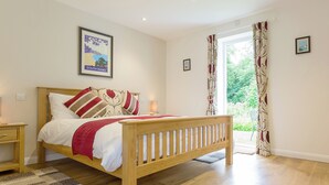 A bedroom with a wooden bed, a nightstand, a framed picture on the wall, and a window with curtains. - 2 bedroom accommodation in Loddiswell Station, near Kingsbridge (Loddiswell Station, near Kingsbridge)