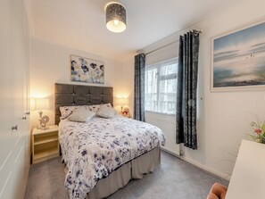 A bedroom with a bed, bedside lamps, a window with curtains, a painting, and a view of the outdoors.