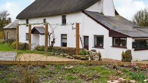 Een wit huis met rieten dak, stenen fundering en een tuin vol bloemen en planten.