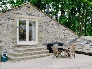 A stone building with a white door and windows, a small outdoor seating area with a table and chairs, and a chimney.