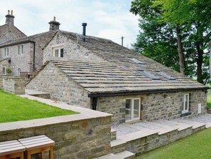 A stone building with a sloped roof, a wooden bench, and a grassy area.