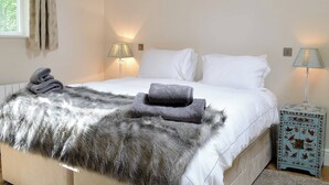 Un lit bien fait, avec du linge de lit blanc, deux lampes de chevet, un plaid gris moelleux et une petite table d’appoint bleue ornée de motifs floraux.