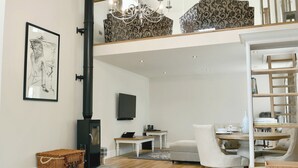 Un espace de vie moderne de style loft, doté d’un haut plafond, d’une cheminée, d’un coin repas et d’un lit en mezzanine.