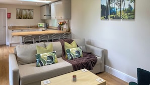 Una sala de estar moderna con un sofá, una mesa de centro y una zona de comedor con sillas, y una cocina al fondo.