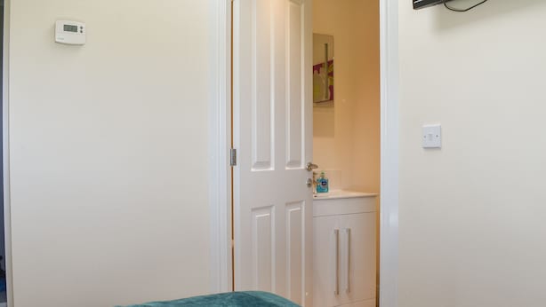 Un dormitorio con cama, una puerta blanca, un armario blanco y un termostato fijado a la pared.