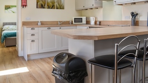 Una cocina moderna con encimera de madera, armarios blancos, una campana de acero inoxidable, un microondas y una cafetera.