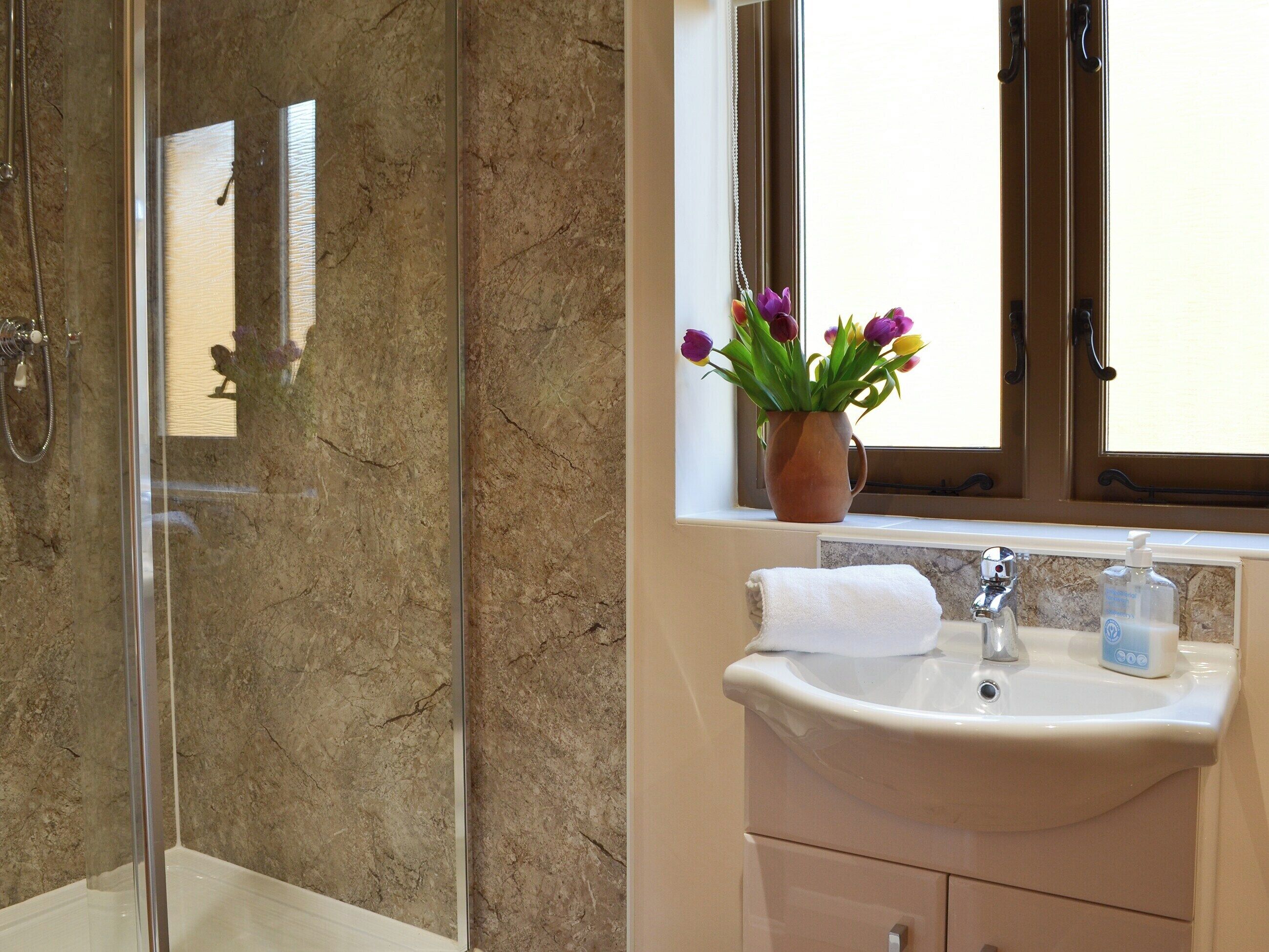 A bathroom with a glass shower enclosure, a sink with a vase of flowers, and a window above the sink.
