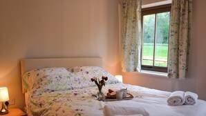 Una cama bien hecha con ropa de cama floral, una mesita de noche con lámpara y una ventana con cortinas.