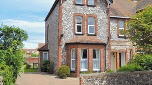 Une maison à deux étages avec une façade en pierre, un toit en tuiles et un petit jardin à l’avant.