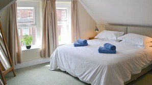 Une chambre à coucher avec un grand lit, une fenêtre avec des rideaux, une petite plante en pot et une lampe sur une table de chevet.