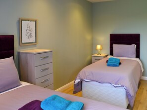 Une chambre d’hôtel avec deux lits, une table de chevet avec une lampe, une commode et une estampe botanique encadrée au mur.