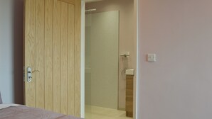 A bedroom with a wooden wardrobe, a bed with a white cover, and a bathroom with a glass shower enclosure. - Aimmee's Lodge - UKC2203 (Doddington, near Lincoln)
