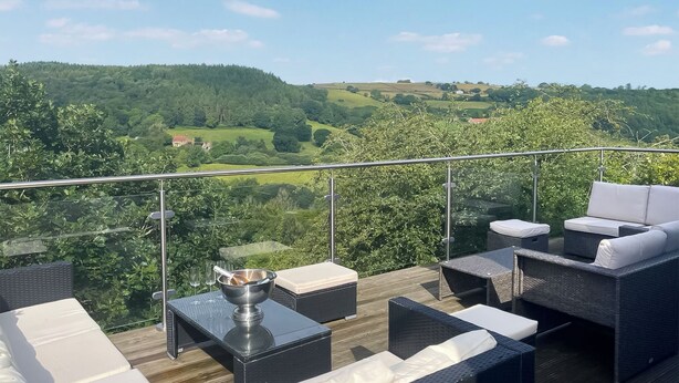 A balcony with wicker furniture, a glass table, and a metal bowl. - 4 bedroom accommodation in Beck Hole, near Whitby (Beck Hole, near Whitby)