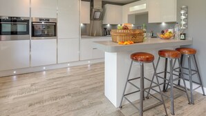 A modern kitchen with white cabinetry, stainless steel appliances, and a central island with stools. - 4 bedroom accommodation in Beck Hole, near Whitby (Beck Hole, near Whitby)
