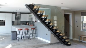 A modern kitchen with a central island, a staircase with glass railings, and a dining area with stools. - 4 bedroom accommodation in Beck Hole, near Whitby (Beck Hole, near Whitby)