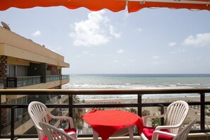 A balcony with a table and two chairs, overlooking a beach and ocean.