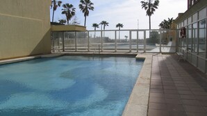 Une piscine dotée d’une terrasse carrelée, entourée d’une rambarde en verre et de palmiers.
