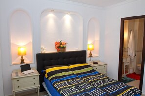 A bedroom with a bed, two bedside tables, a laptop, and wall-mounted lamps.