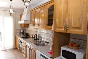 Una cocina con armarios de madera, microondas, lavamanos y cafetera.
