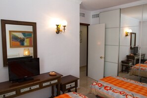 A hotel room with a television on a wooden dresser, a mirror, and a bed with an orange and white bedspread.