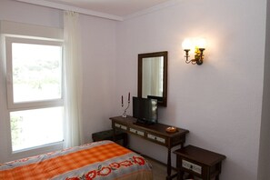 Habitación de hotel con cama, cómoda, televisor y lámpara fijada a la pared.