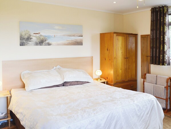 A bedroom with a bed, a nightstand, a lamp, a wooden wardrobe, and a painting on the wall.