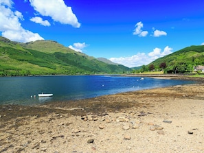 A lake with a boat, rocky shore, and green hills in the background. - 2 bedroom accommodation in Sallachy, near Dornie (Sallachy, near Dornie)