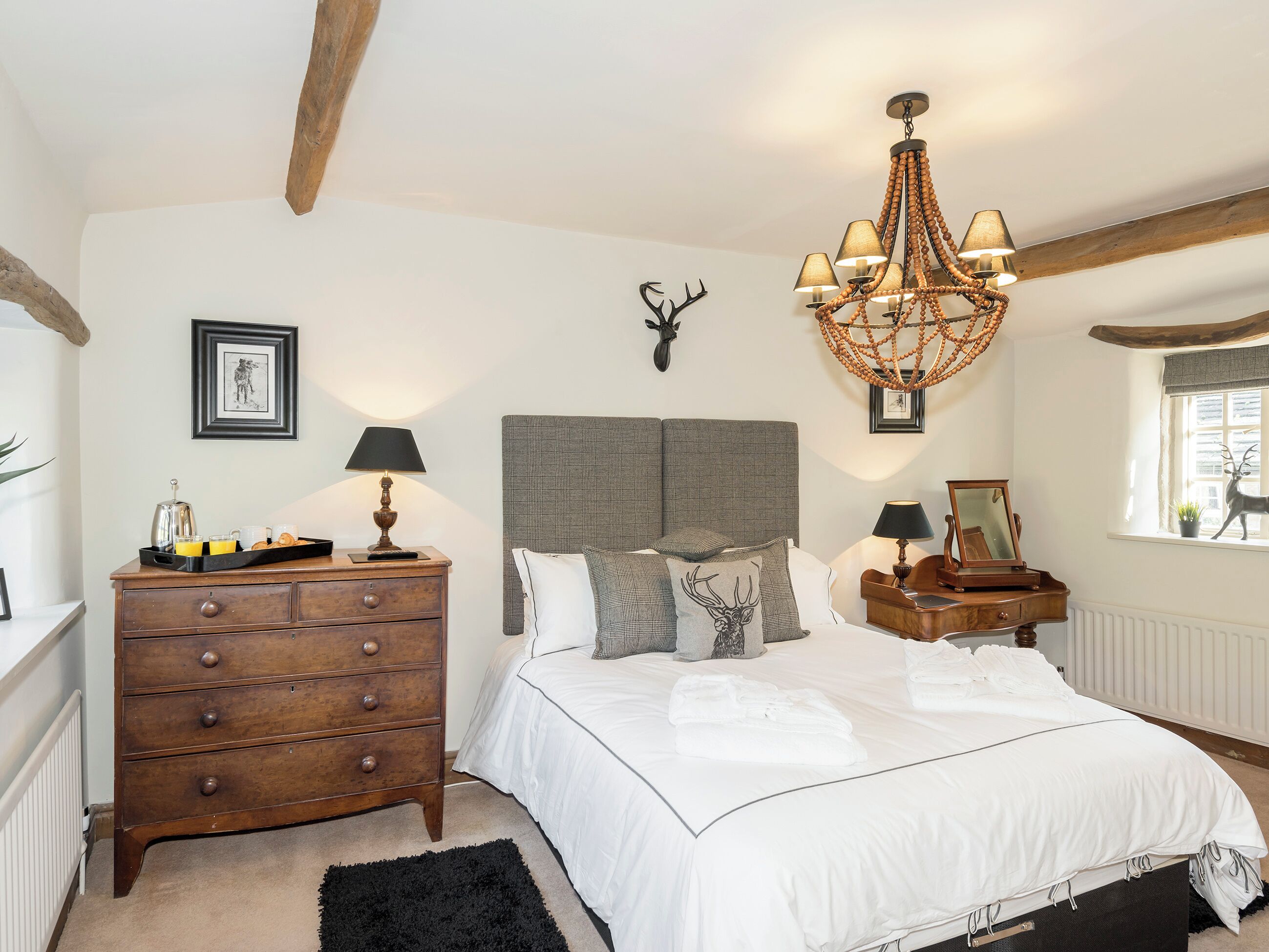 A bedroom with a bed, dresser, nightstands, a chandelier, and a window with a deer decoration.