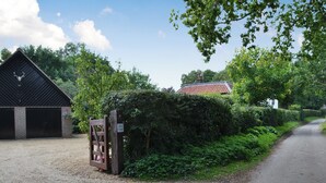 A rural property entrance with a gravel driveway leading to a brick building, a wooden gate, and a sign indicating 'Broad Cottages'. - Broad Cottage Boathouse (Ranworth, near Wroxham)