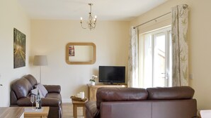 Un salon avec un canapé en cuir marron, une table basse en bois, un téléviseur à écran plat, une lampe et une grande fenêtre avec des rideaux.