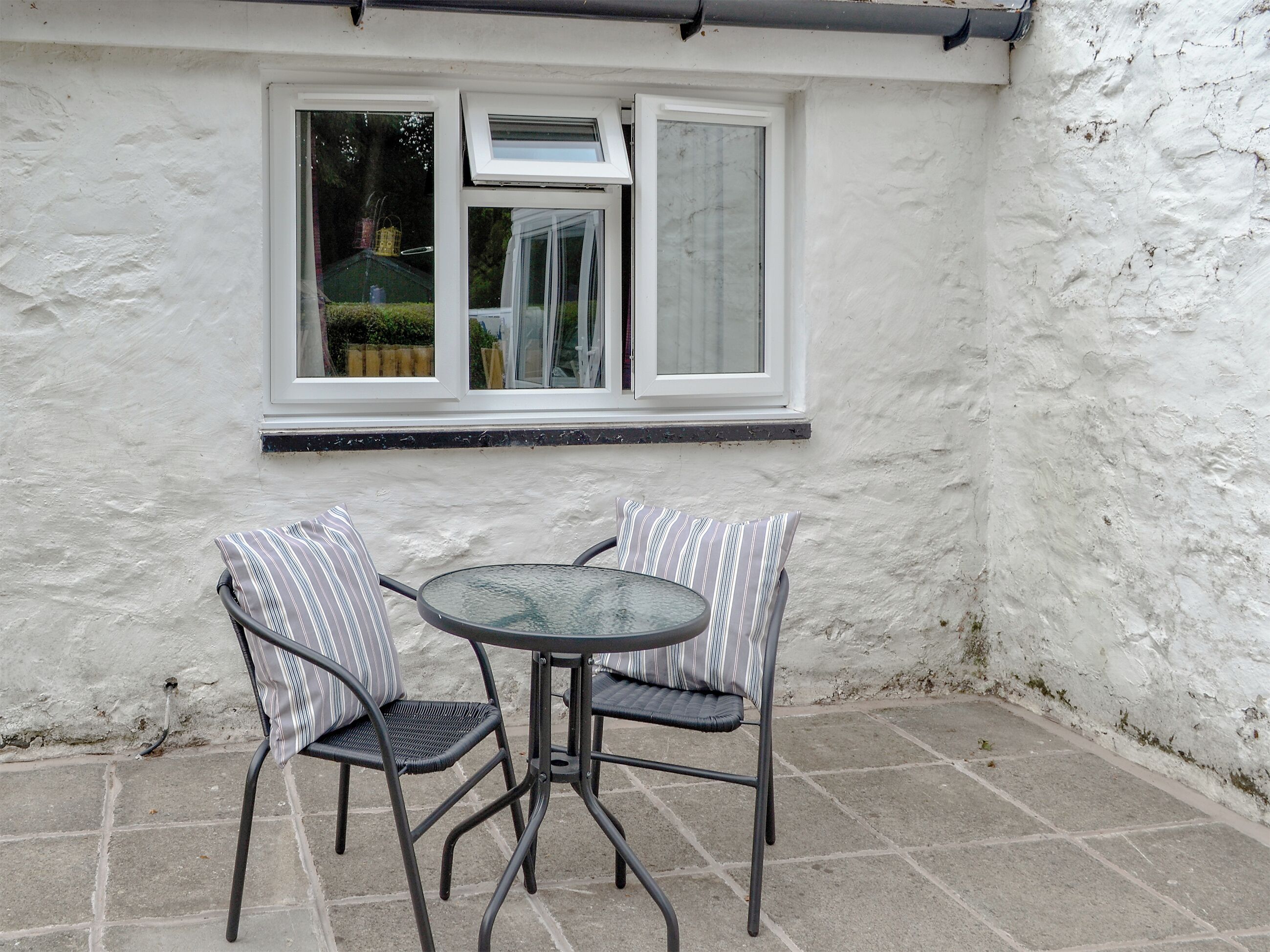 A patio with two chairs and a table, a white exterior wall, and a window with blinds.