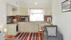 A compact kitchen with a microwave, toaster, and oven. There is a dining area with a table and chairs, and a grey sofa with striped cushions.