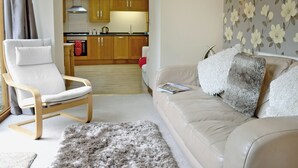 A living room with a sofa, a chair, a fluffy rug, and a kitchen in the background. - 2 bedroom accommodation in Swan Pool, near Falmouth (Swan Pool, near Falmouth)