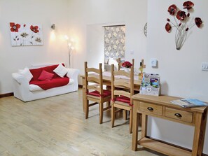 A cozy living room with a white sofa, red cushions, a wooden dining table with chairs, and a small wooden desk with a chair.