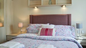 Ein ordentlich bezogenes Bett mit Blumenmuster, einem Kopfteil, Nachttischlampen und einem Regal darüber.