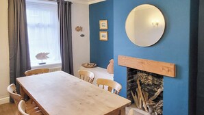 Une salle à manger avec une table et des chaises en bois, une cheminée et un mur bleu orné de tableaux encadrés.