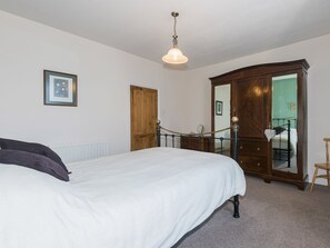 A bedroom with a bed, a wooden wardrobe, a mirror, and a hanging light fixture. - 3 bedroom accommodation in Haverigg, near Millom (Haverigg, near Millom)