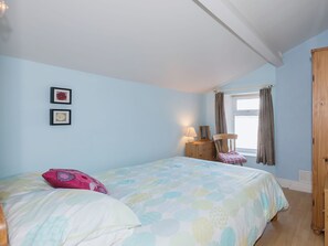 A bedroom with a bed, a nightstand, a chair, a window with curtains, and two framed pictures on the wall. - 3 bedroom accommodation in Haverigg, near Millom (Haverigg, near Millom)