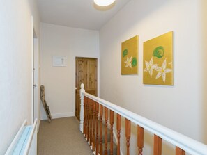 A hallway with a wooden staircase, white walls, and two yellow paintings with green leaves.