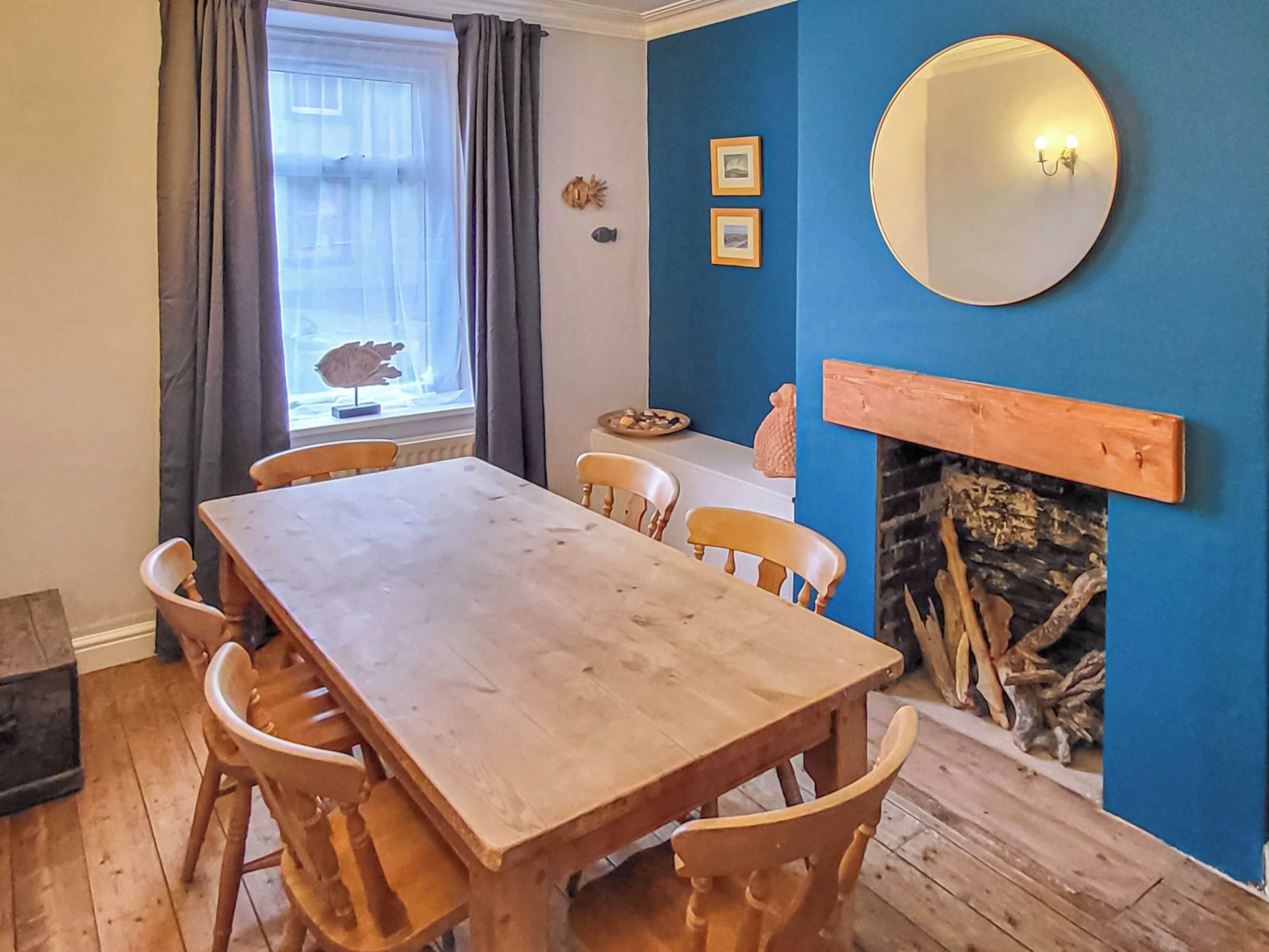 A dining room with a wooden table and chairs, a fireplace, and a blue accent wall.