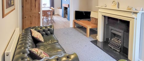 Una sala de estar con un sofá de cuero negro, una chimenea y un comedor al fondo.