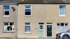 Un immeuble de deux étages doté d’une façade à motifs, d’une porte verte et d’une voiture garée.