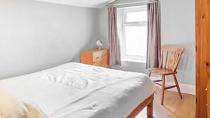 Un dormitorio con una cama, un aparador de madera, una silla y una ventana con cortinas.