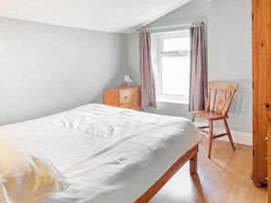 Une chambre à coucher avec un lit, une commode en bois, une chaise et une fenêtre avec des rideaux.
